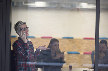 Image showing business woman at office speaking by phone  team on meeting in b