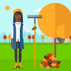 Image showing Woman with rake near tree and heap of leaves.