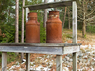 Image showing two old rusty milk jug on a bench