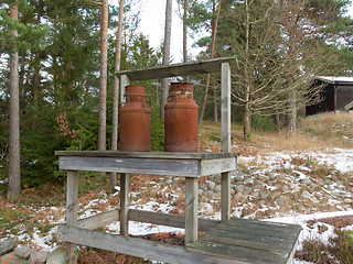 Image showing two old rusty milk jug on a bench 