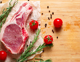 Image showing Pieces of crude meat with rosemary and tomatoes.