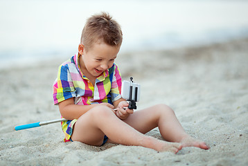 Image showing Happy boy with selfie stick and cell at the seaside