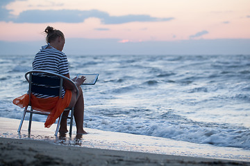 Image showing Woman sitting on chair by sea and using pad