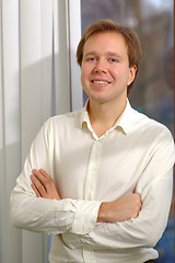 Image showing Young smiling man with folded arms by the window