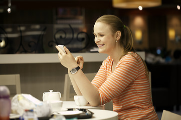 Image showing Young woman chatting on smartphone in cafe.