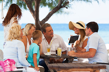 Image showing Family looking at photo on touch pad in outdoor cafe