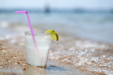 Image showing Glass of lemonade or water on beach by sea
