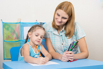 Image showing The five-year child draws on a sheet of paper, next to the teacher holds pencils