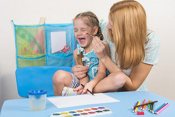 Image showing Mother tickles the cheek with a brush to paint his daughter, five-year