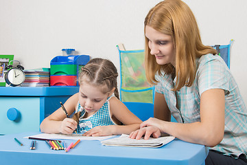 Image showing The girl draws in a notebook with a ruler, the teacher helps her