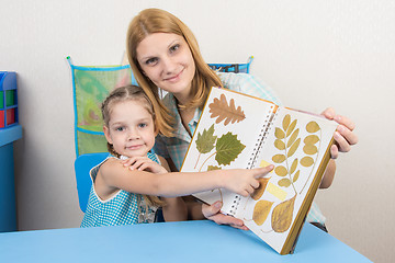 Image showing Five-year girl and mother examining herbarium shows on one of the sheets in the album, and looked into the frame