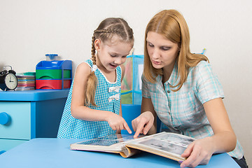 Image showing Five-year girl and mother looking at the photos in the album at the table at home