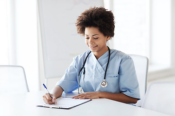 Image showing happy female doctor or nurse writing to clipboard