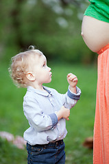 Image showing Cute little boy looking at pregnant moms belly