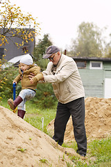 Image showing Grandpa helps grandson to get on a sand hill