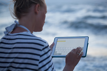 Image showing Woman typing on tablet PC by sea