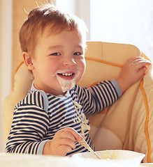 Image showing Two year old boy smiles and eating porridge.