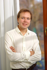 Image showing Happy young man standing by the window with blinds