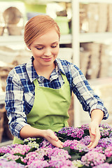 Image showing happy woman taking care of flowers in greenhouse