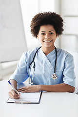 Image showing happy female doctor or nurse writing to clipboard