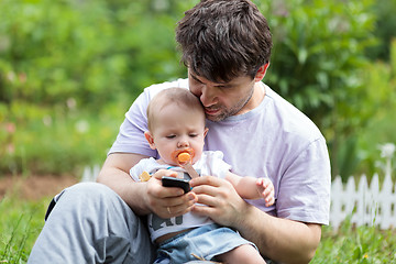 Image showing Father holding a baby and texting on his mobile