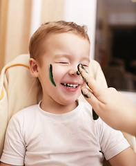 Image showing Little boy laughing as his mother paints his face