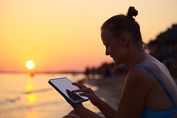 Image showing Smiling woman using pad on beach at sunset