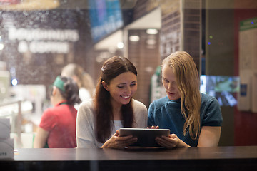 Image showing Two women talk cheerfully in the restaurant using electronic tablet