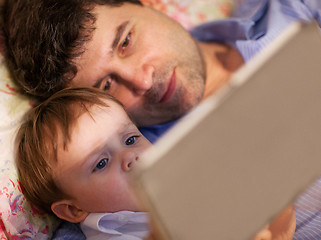 Image showing Man and little boy playing with tablet in bed