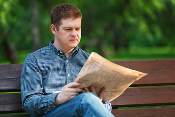 Image showing Man reads newspaper on bench in the park