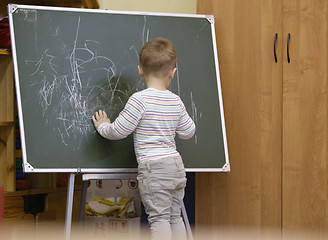 Image showing Little boy drawing on a chalkboard at kindergarten