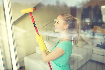 Image showing happy woman in gloves cleaning window with sponge