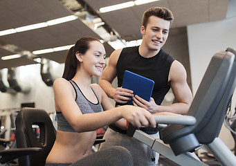 Image showing happy woman with trainer on exercise bike in gym