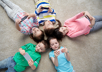 Image showing happy children with smartphones lying on floor