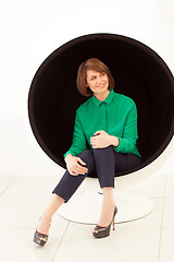 Image showing Red haired smiling woman looking away while sitting on modern chair