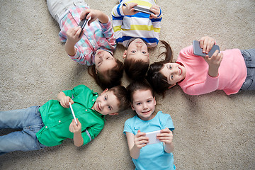 Image showing happy children with smartphones lying on floor