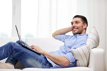 Image showing smiling man lying on couch with laptop at home