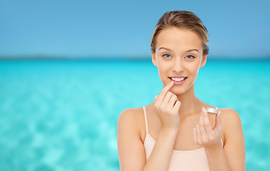 Image showing smiling young woman applying lip balm to her lips