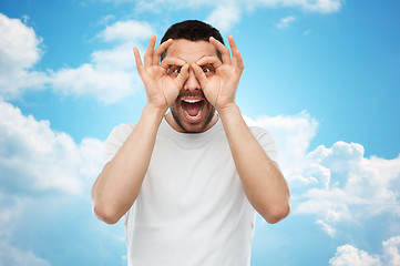 Image showing man making finger glasses over blue sky