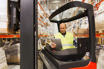 Image showing man with tablet pc operating forklift at warehouse