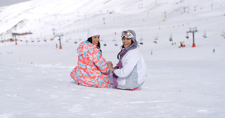 Image showing Two young women sitting in snow at a ski resort