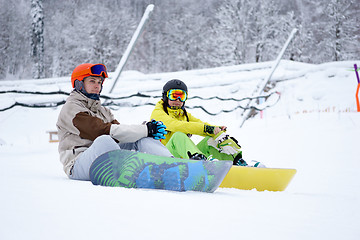 Image showing Two snowboarders - men and women sitting in the mountains
