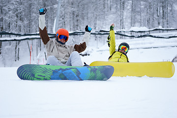 Image showing Two snowboarders - men and women sitting in the mountains