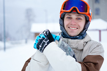 Image showing Man snowboarder wearing orange helmet, grey jacket, black and blue gloves standing with snowboard