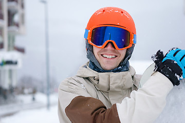 Image showing Man snowboarder wearing orange helmet, grey jacket, black and blue gloves standing with snowboard