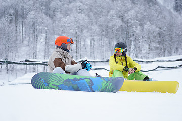 Image showing Two snowboarders - men and women sitting in the mountains