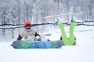 Image showing Two snowboarders - men and women sitting in the mountains