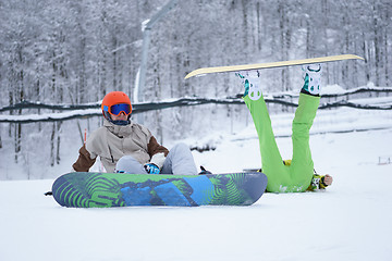 Image showing Two snowboarders - men and women sitting in the mountains