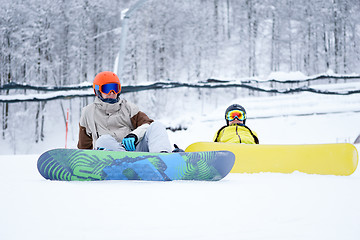 Image showing Two snowboarders - men and women sitting in the mountains