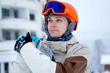 Image showing Man snowboarder wearing orange helmet, grey jacket, black and blue gloves standing with snowboard